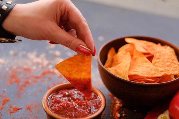 Junk fast food et mauvaise alimentation nacho tortilla chips dans un bol femme main trempant des chips triangulaires épicées croquantes dans la sauce tomate salsa