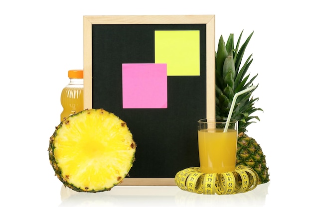 Jus d'ananas frais et ananas mûr avec un tableau noir et un ruban à mesurer sur fond blanc