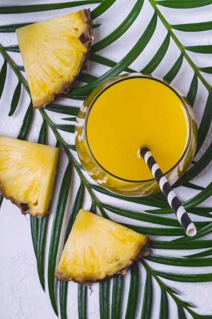 Jus d'ananas et tranches d'ananas sur feuille tropicale