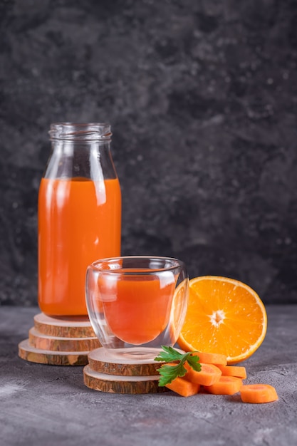 Jus de carotte et d'orange dans une bouteille et verre sur des supports en bois dans un low key