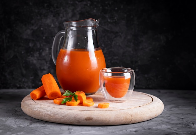 Jus de carotte et d'orange dans une cruche sur une planche ronde en bois en discret