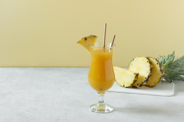 Jus frais d'ananas en verre sur table en béton gris sur fond jaune