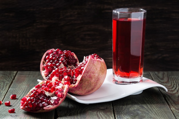 Jus de grenade en verre et tranches de grenade mûre avec des grains sur une table en bois