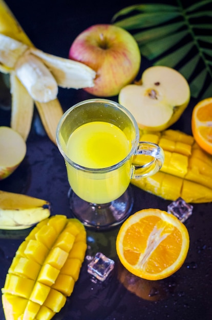 Jus multifruits avec des fruits autour sur fond noir avec congé tropical