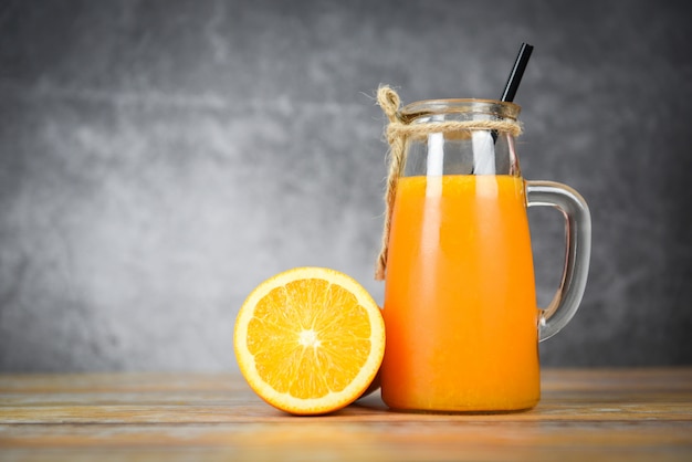 Jus d'orange dans le bocal en verre et une tranche de fruit orange fraîche sur une table en bois