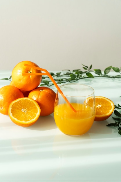 Jus d'orange dans un verre entouré d'oranges naturelles et de quelques feuilles vertes avec un fond blanc lumière du soleil naturel