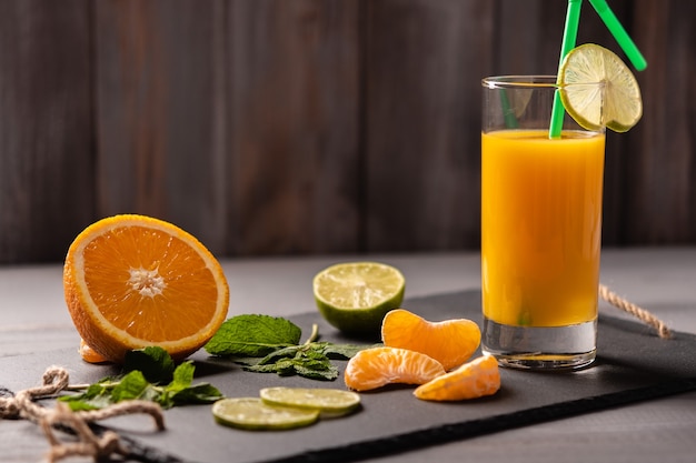 Jus d'orange dans un verre avec tube sur un tableau noir sur un fond en bois foncé près de la menthe orange