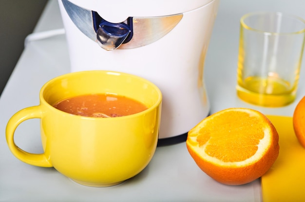 jus d'orange fraîchement pressé dans une tasse jaune orange fraîchement coupée et presse-agrumes sur le tableau blanc