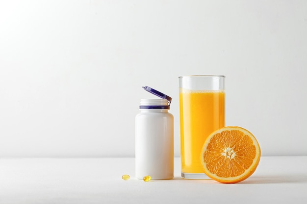 Jus d'orange frais dans un verre et une bouteille de vitamines sur tableau blanc. Carence en vitamines