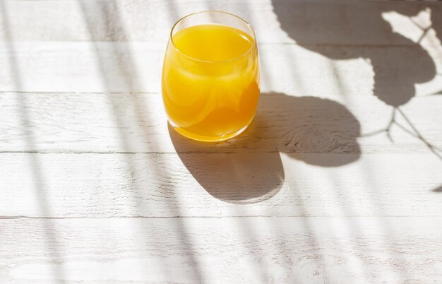 Jus d'orange frais dans un verre sur la table en bois blanche avec des ombres dures un jour d'été