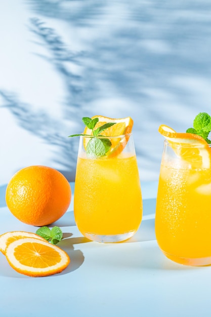 Jus d'orange frais avec de la glace dans un verre sur un cocktail orange de fond bleu
