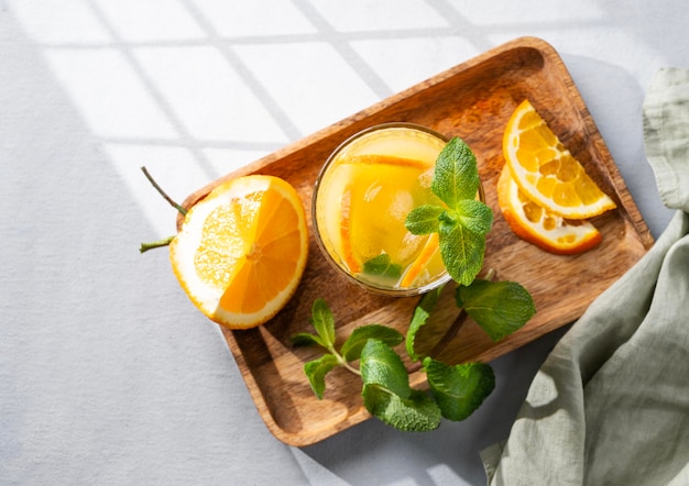 Jus d'orange avec des fruits frais, de la menthe et de la glace sur un fond clair avec de l'ombre et une serviette Boisson de désintoxication d'agrumes fraîchement pressée pour le petit déjeuner