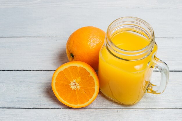 Jus d'orange et jus tranchés sur fond en bois blanc