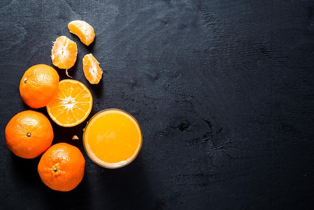 Jus d'orange en verre avec des oranges crues sur fond noir. Copier l'espace