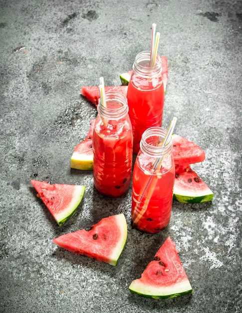 Jus de pastèque en bouteilles avec des pailles sur table rustique.