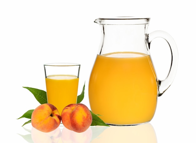 Jus de pêche dans un verre et une carafe avec des pêches sur fond blanc