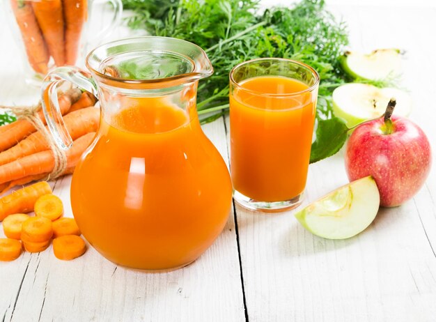 Jus de pomme de carotte et carottes et pommes fraîches sur le fond en bois