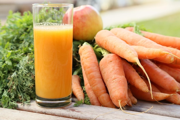 Jus de pomme carotte frais dans un verre sur une surface en bois. Carottes et pommes en arrière-plan