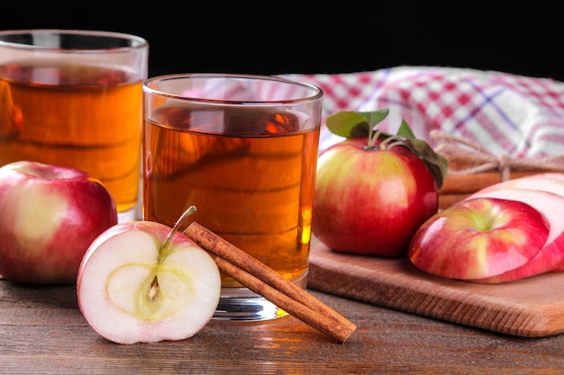 Jus de pomme dans un verre avec beaucoup de pommes rouges fraîches et de cannelle sur une table en bois marron sur fond noir