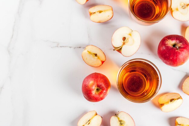 Jus de pomme ferme biologique frais dans des verres avec des pommes rouges entières et tranchées crues, sur une table en marbre blanc, copyspace vue de dessus