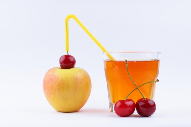 Jus avec des pommes et des cerises Jus de pomme frais dans un verre sur fond blanc Pommes et cerises pour la fabrication de jus Concept de boisson saine