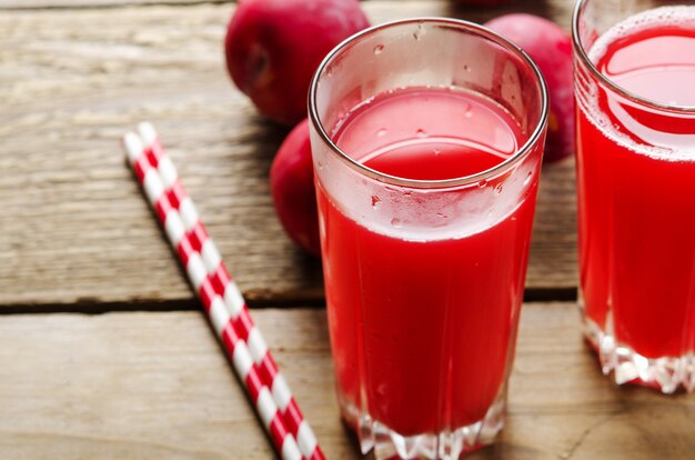 Jus de prune dans des verres en verre avec des prunes et des pailles pour le jus sur la table en bois