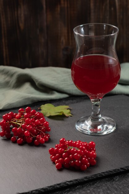 Jus rouge de viorne dans un verre sur une tige sur une table sombre. Près des baies de viorne et de la serviette en lin. La nourriture saine. Espace de copie