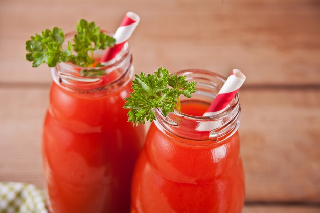 Jus de tomate en bouteille avec du persil et du sel sur la table en bois