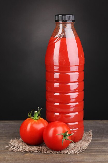 Jus de tomate en bouteille sur table en bois sur fond gris