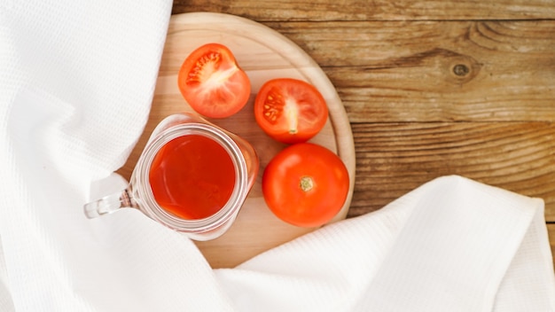 Jus de tomate dans un bocal en verre et tomates fraîches sur une planche à découper en bois et une serviette blanche