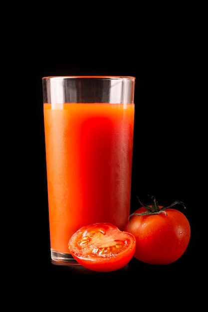 Jus de tomate dans un grand verre en verre avec des tomates fraîches naturelles sur fond noir