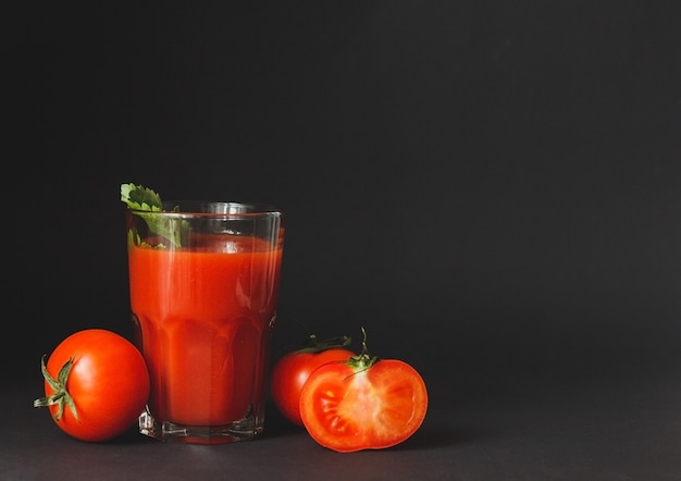 Jus de tomate dans un verre avec des tomates fraîches sur fond noir