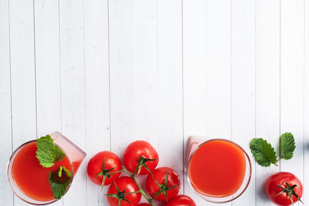 Jus de tomate dans des verres en verre et tomates mûres fraîches sur une branche. Fond en bois blanc avec.