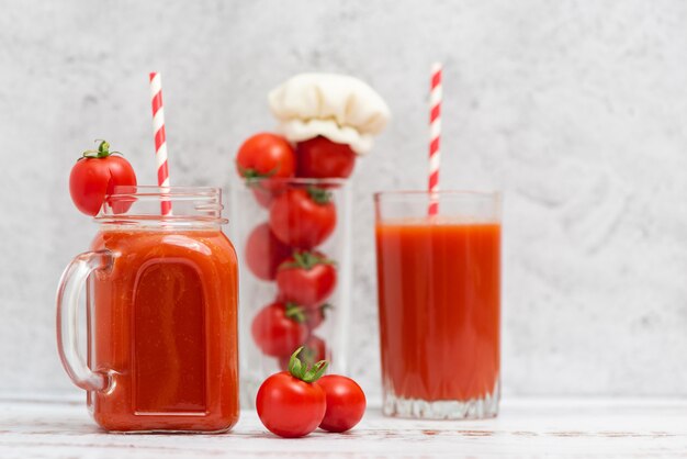 Jus de tomate fraîche dans des verres et tomates cerises sur fond gris