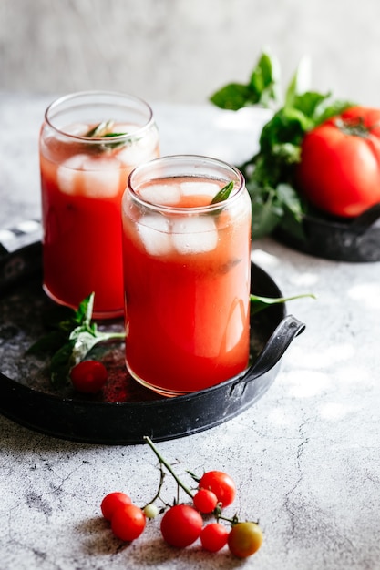 Jus de tomate avec de la glace dans un verre sur fond gris