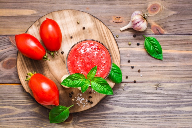 Jus de tomates fraîches au basilic laisse dans des verres et ingrédients pour sa préparation sur une table en bois. Vue de dessus