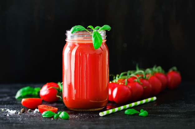 Jus de tomates fraîches biologiques dans un bocal en verre, basilic, cerise, sel, poivre et paille sur noir foncé. Propre concept d&#39;alimentation et de régime.