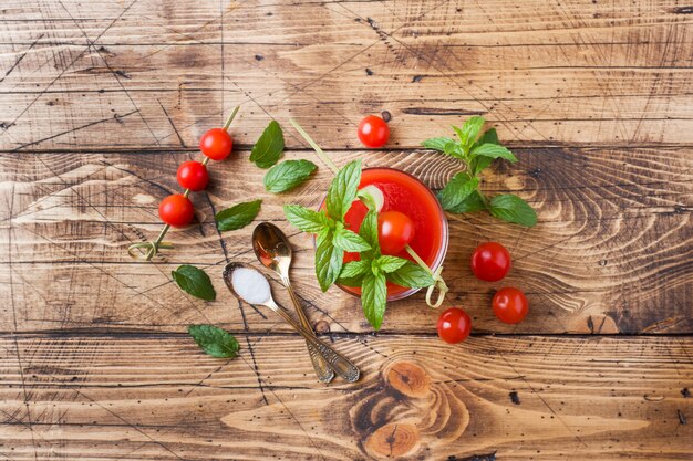 Jus de tomates à la menthe dans un verre et tomates fraîches sur une table en bois. Concept d'aliments biologiques sains.