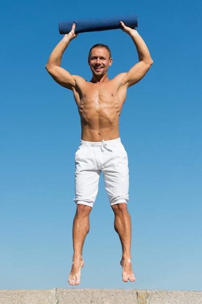 Jusqu'à un mode de vie sain Homme avec tapis de yoga capturé sur fond de ciel en plein air Sportif avec saut de tapis Entraînement en plein air Étirer les muscles après l'entraînement Cours de yoga Pratiquer le yoga ou les étirements