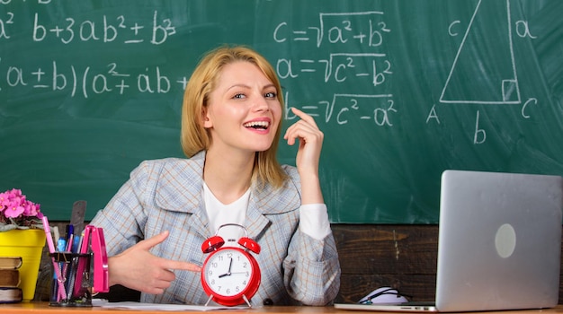 Juste à temps. professeur avec réveil au tableau noir. Temps. femme en classe. Retour à l'école. Le jour du professeur. Étude et éducation. Ecole moderne. Journée du savoir. L'école. Enseignement à domicile. femme joyeuse.