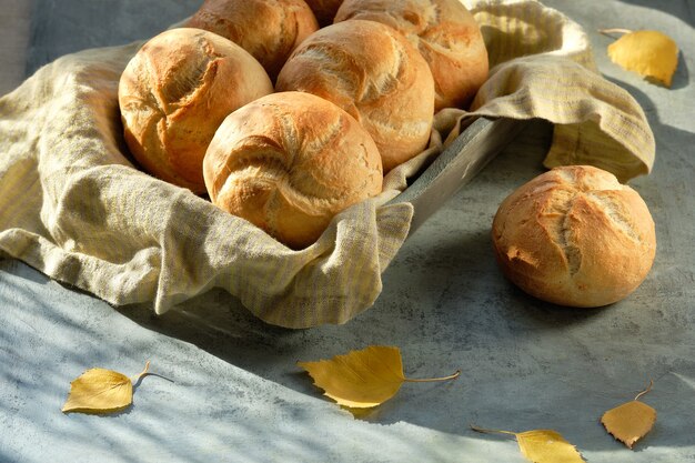 Kaiser, ou petits pains de Vienne dans une corbeille à pain sur fond gris foncé avec des feuilles d'automne jaunes.