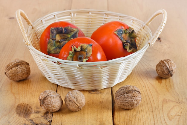 Kakis dans un panier en osier sur une planche de bois