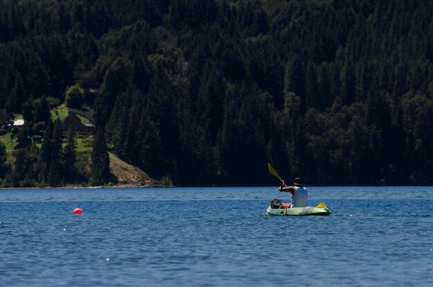 un kayak au milieu du lac avec des montagnes et des forêts en arrière-plan