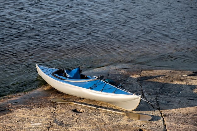 Kayak bleu sur la pierre d'un grand lac Une rame se trouve sur un rivage rocheux Tournant pour attraper du poisson sur la proue du bateau