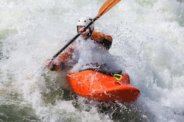 Un kayakiste masculin actif qui roule et surfe dans des eaux agitées