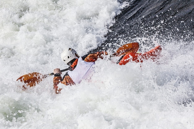 Un kayakiste masculin actif qui roule et surfe dans des eaux agitées