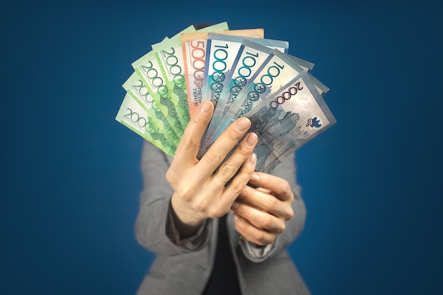 Photo kazakhstan diverses dénominations argent tenge dans les mains sur le fond d'une femme en veste grise
