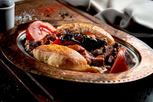 Le kebab Alinazik est un plat d'aubergines grillées et d'agneau dans un petit pain sur une assiette en cuivre. Table noire