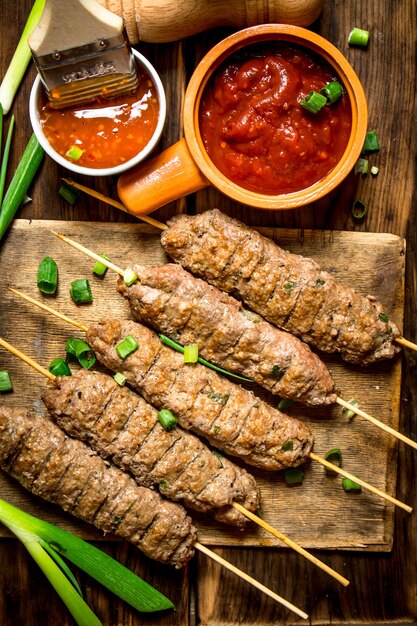 Kebab aux oignons verts et sauce piquante sur table en bois.