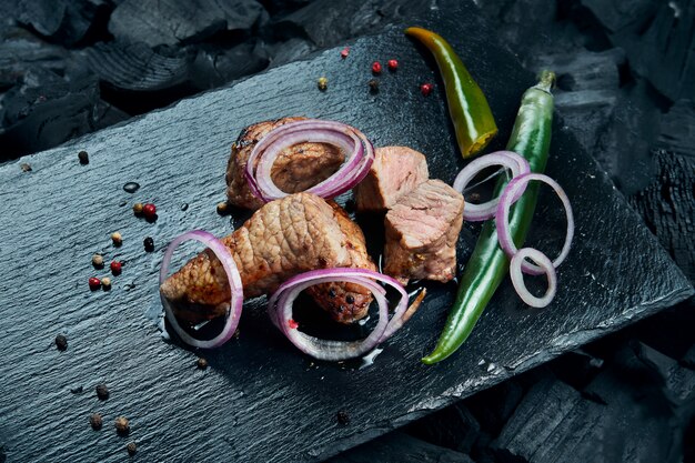 Kebab de boeuf appétissant aux épices et oignons sur un plateau en ardoise noire sur une surface de charbon de bois. Shahlik. Fin, haut, portion, grillé, viande